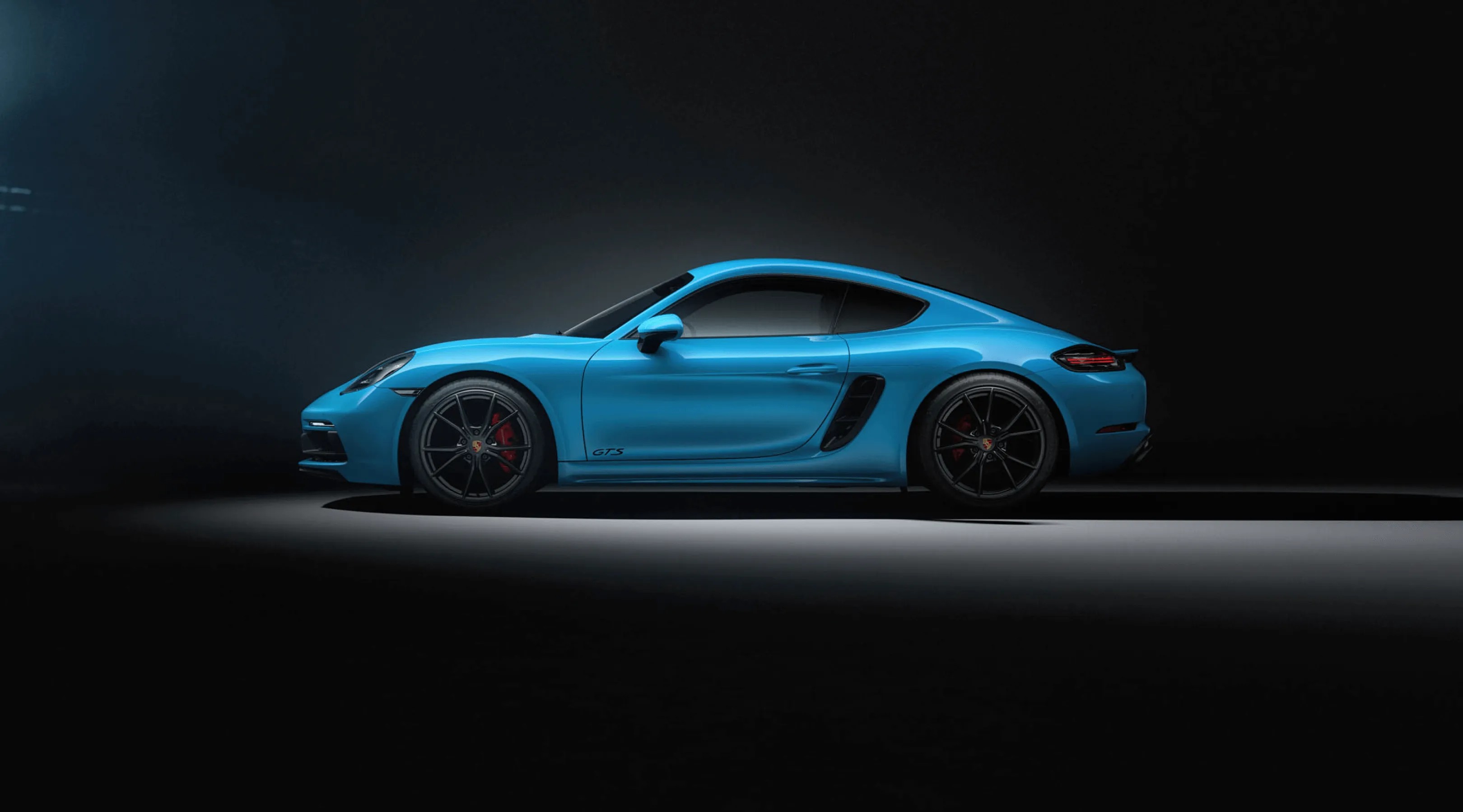 Blue Porsche 911 GTS sports car in a dark studio with spotlight highlighting its side profile.