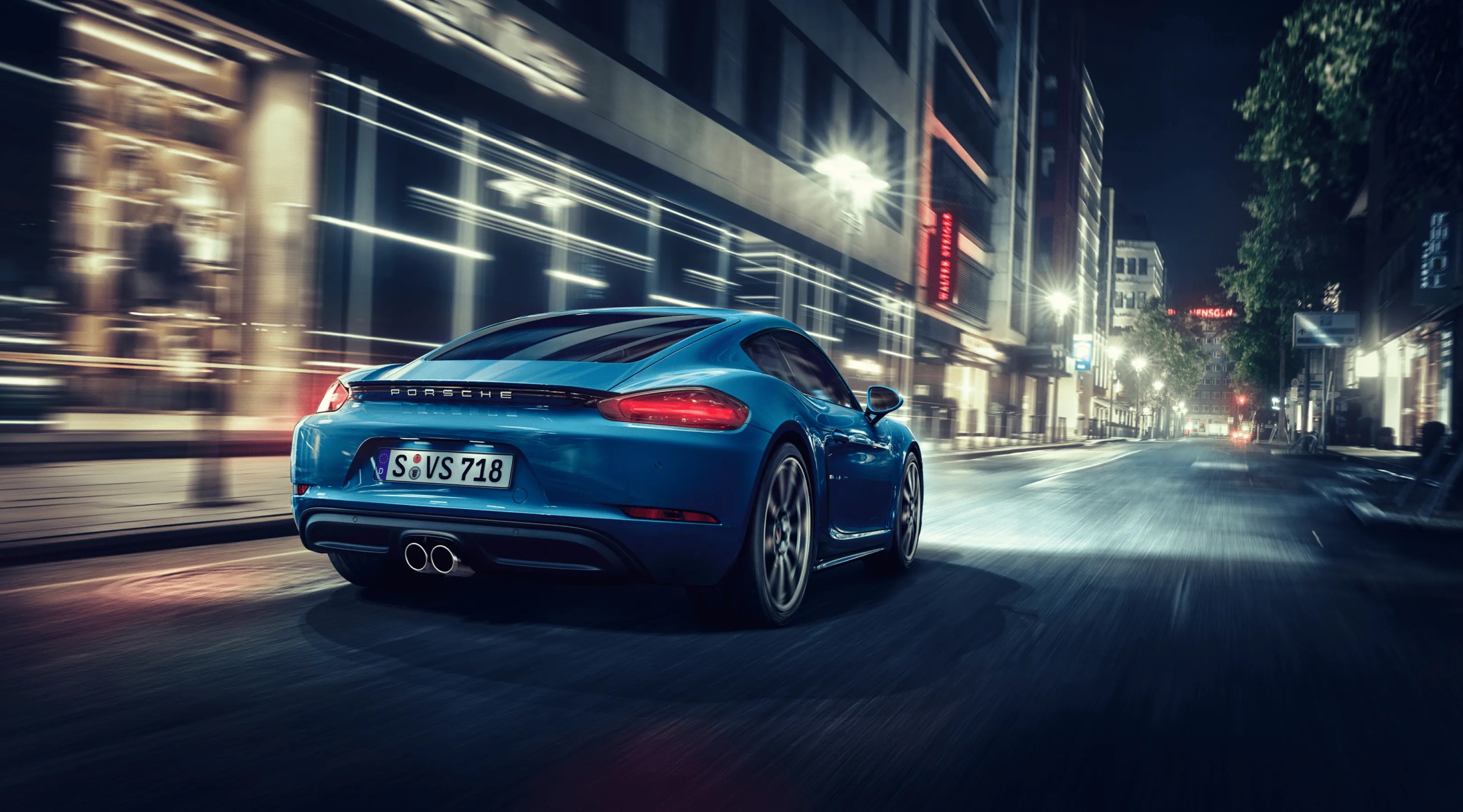 Blue Porsche sports car driving on an empty city street at night with motion blur.